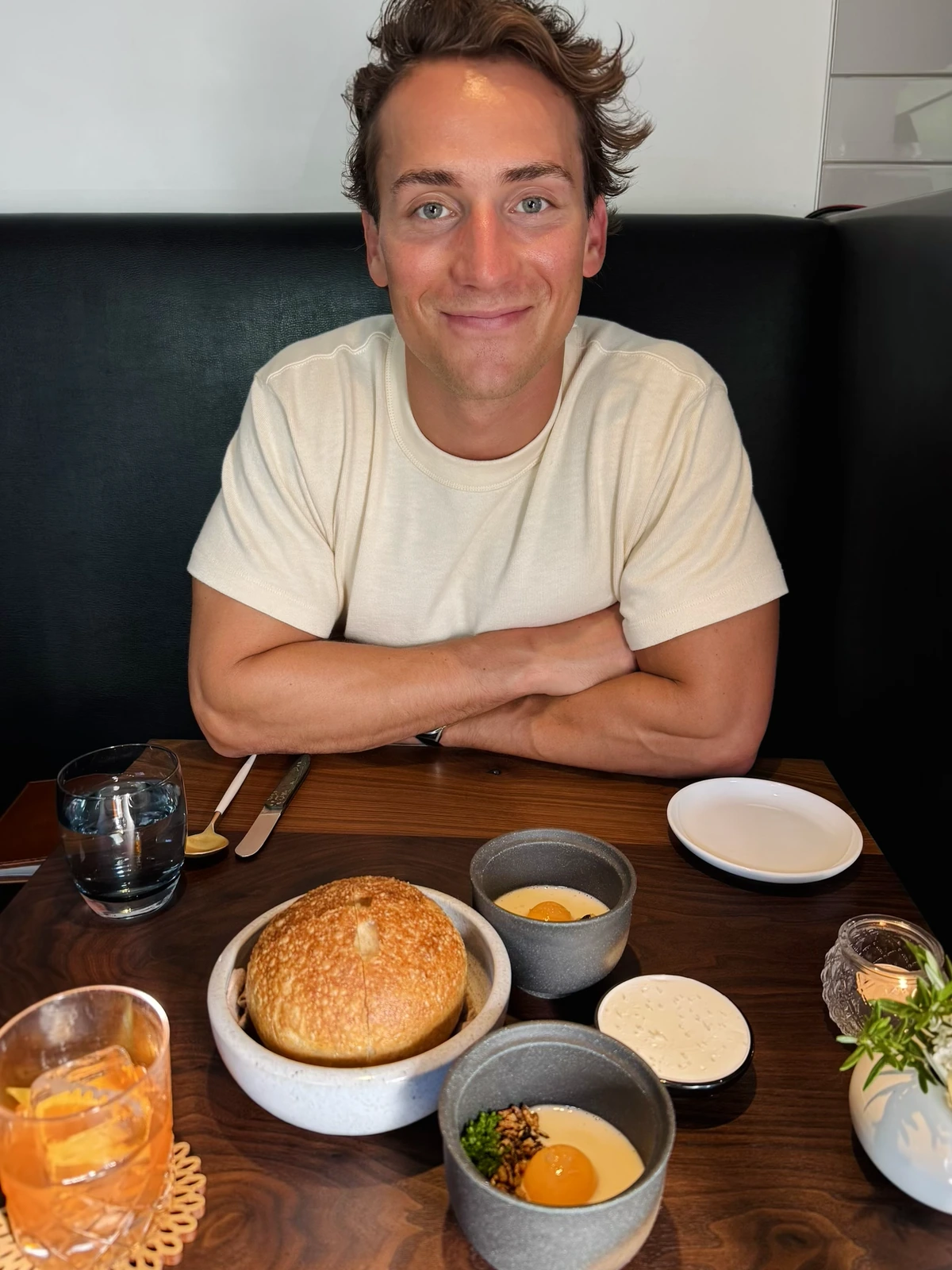 Jarod Farchione seated at a restaurant table set with bread, small savory custards, and a cocktail.